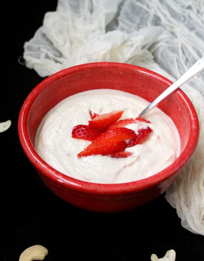 Vegan Cultured Cashew Yogurt in a red bowl with strawberries and a cheesecloth next to it.