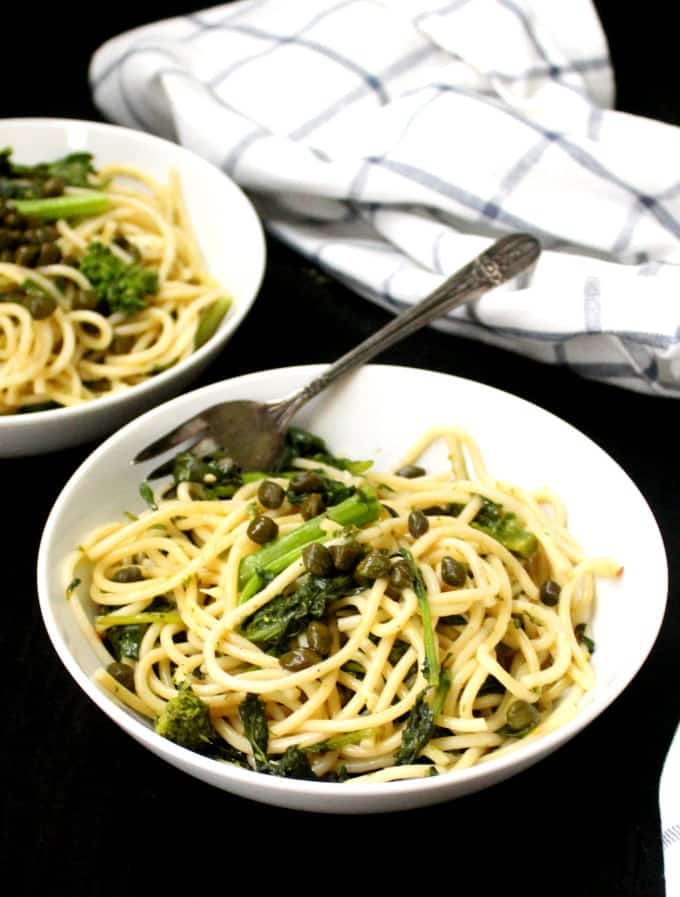 Photo of Vegan Garlicky Pasta with Broccoli Rabe and capers in white bowls with  a fork.