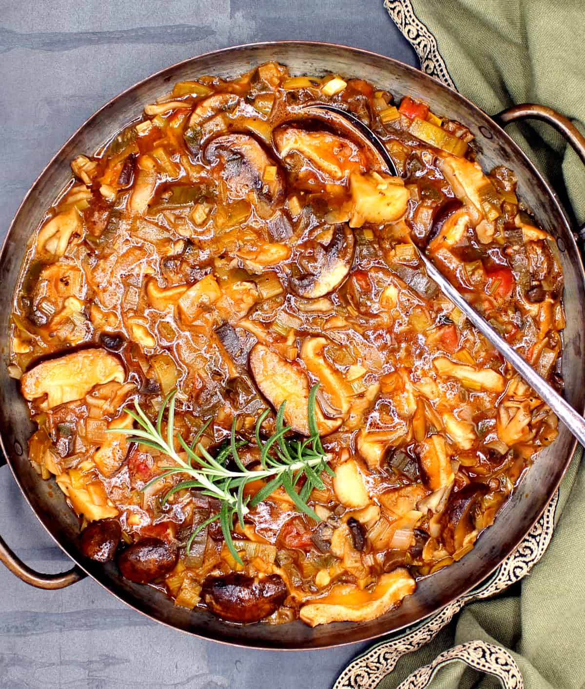 Mushroom stew in pan with rosemary sprigs and spoon.