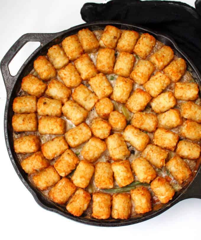Vegan tater tot casserole in cast iron griddle with crispy tater tots.