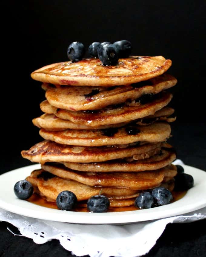 Vegan Sourdough Blueberry Pancakes stacked on white plate with blueberries.