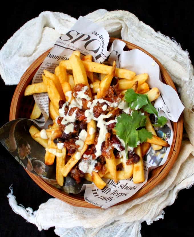 Vegan Chili Fries drizzled with a creamy, cheezy horseradish sauce in basket lined with newspaper.