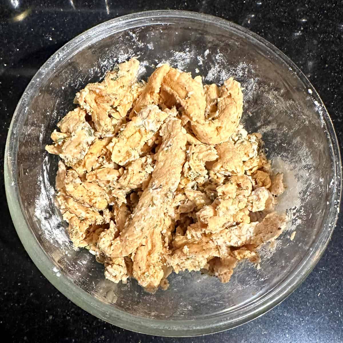 Soy curls coated with flour and herbs in glass bowl.