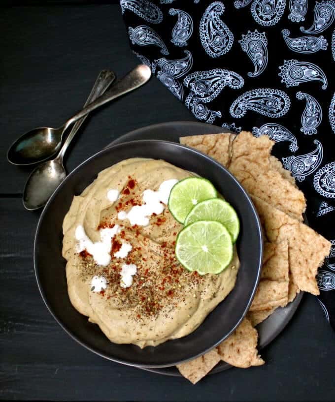 Top shot of Roasted Eggplant Hummus with Za'atar Spice Mix in a black bowl against a gray background and with two spoons - HolyCowVegan.net