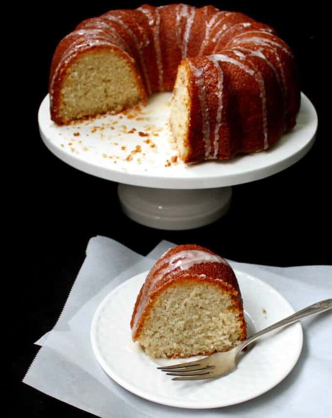 Vegan Lemon Yogurt Bundt Cake on a cake stand with a slice in a white plate with fork.