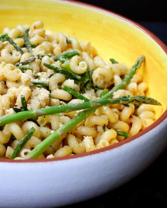 Vegan parmesan sprinkled over Garlicky Pasta with Asparagus and Cashew Parm in a yellow and white bowl.