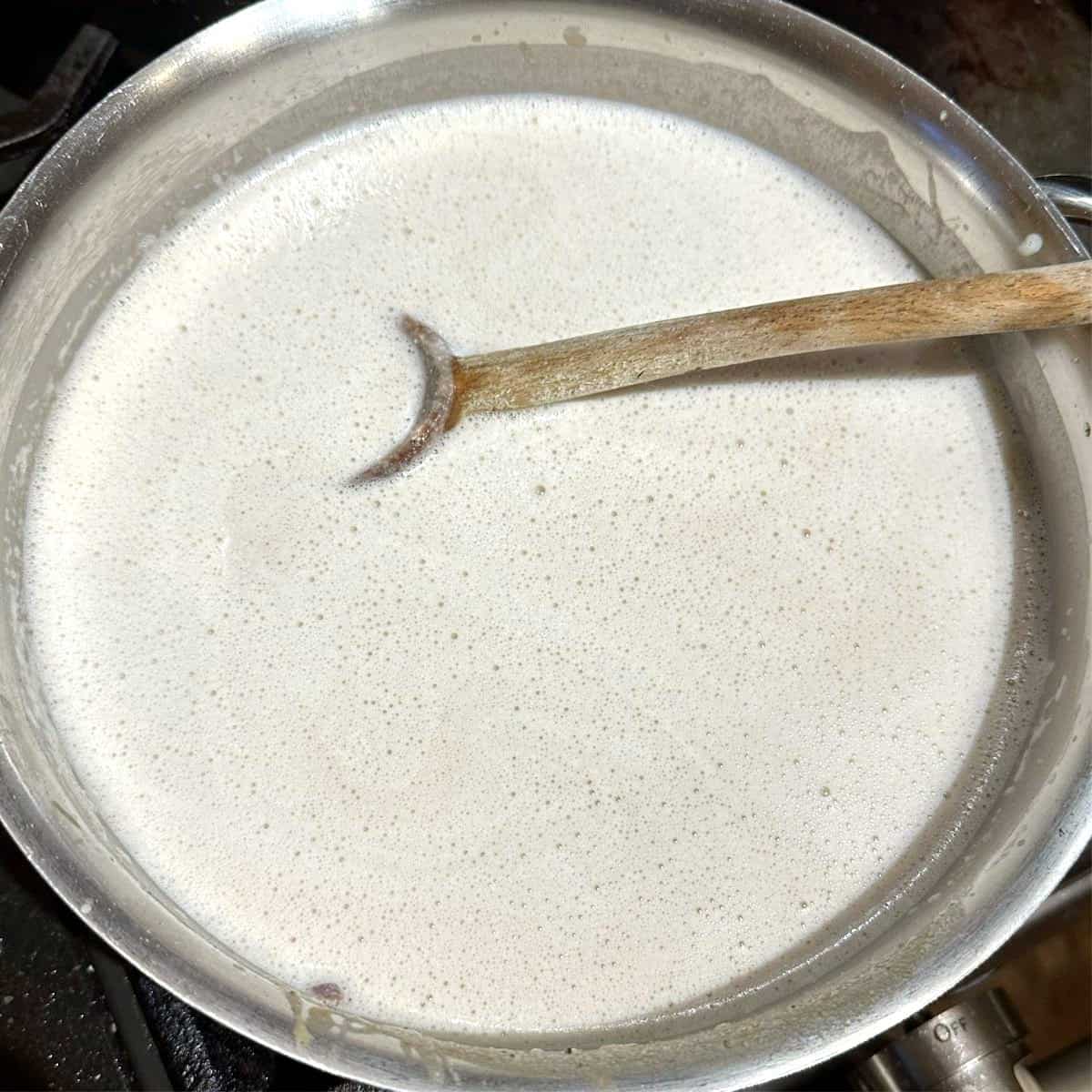 Cashew milk added to saucepan with ladle.
