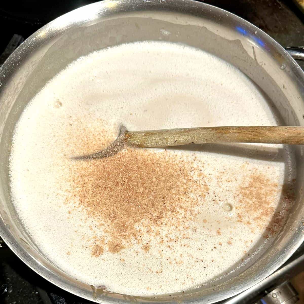 Nutmeg added to cashew milk in saucepan for vegan bechamel.