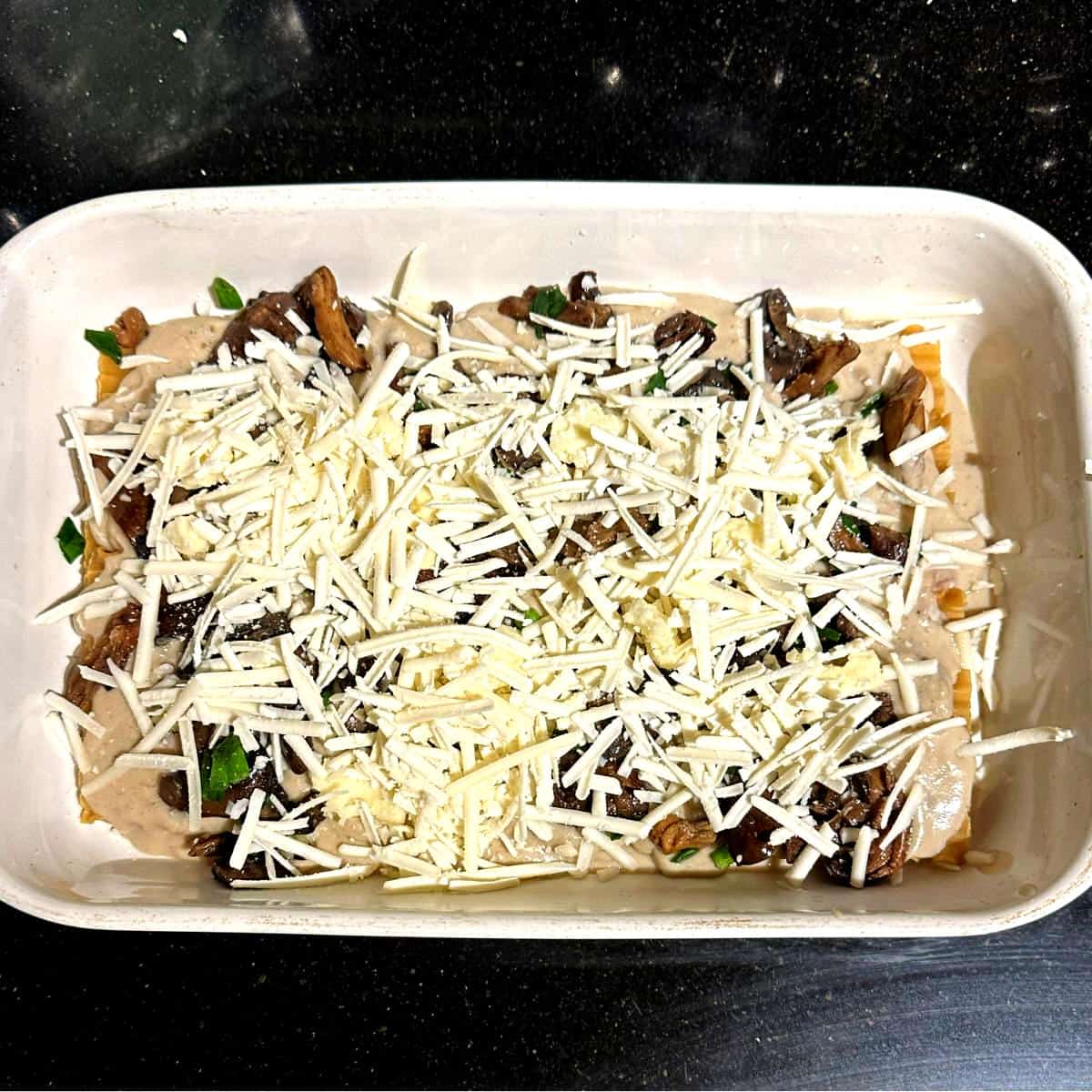 Parmesan and mozzarella scattered over mushroom layer in lasagna pan.
