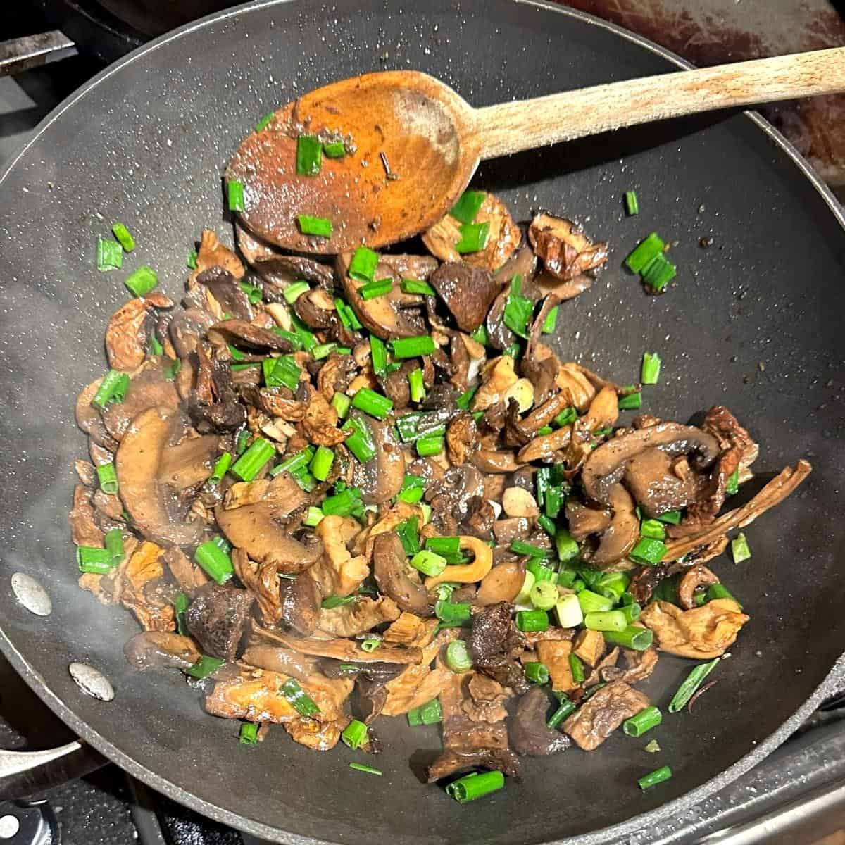 Scallions added to mushrooms in skillet or wok.
