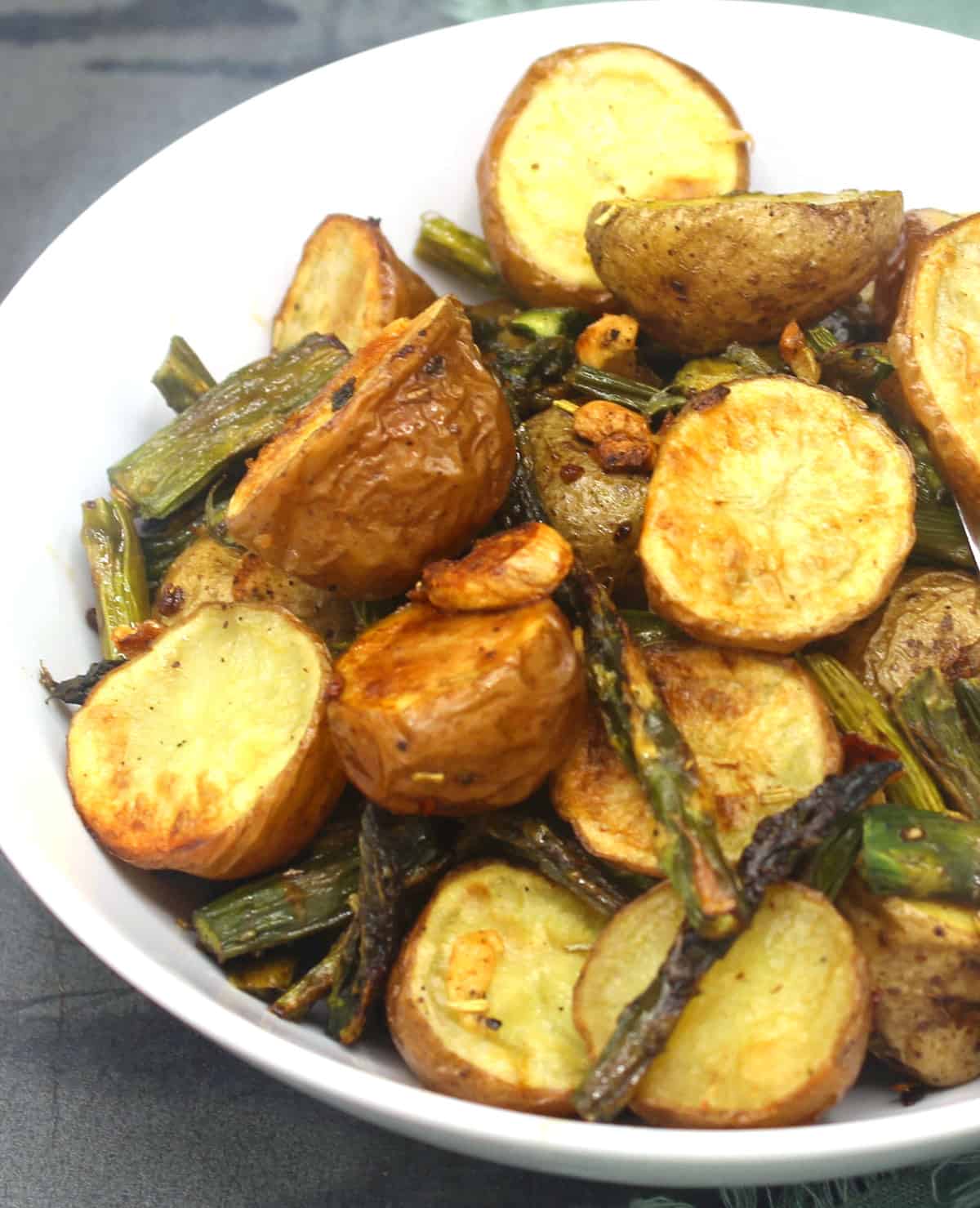 Roasted asparagus and potatoes with garlicky bits in white bowl.