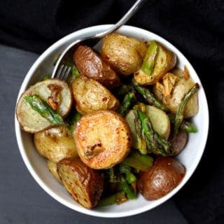 A bowl with garlic roasted asparagus and potatoes with a spoon.