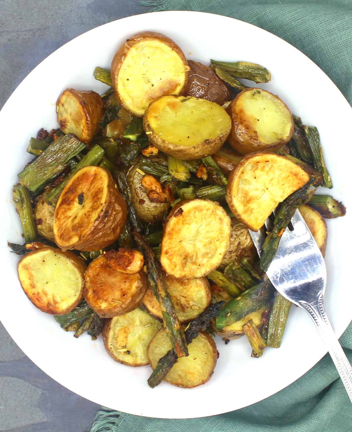 Roasted asparagus and potatoes in white bowl with fork.
