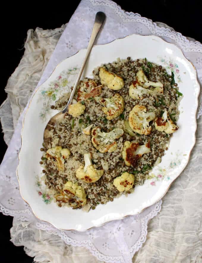 A platter with cauliflower, couscous, lentils and mint with a silver spoon on a lace tablecloth.