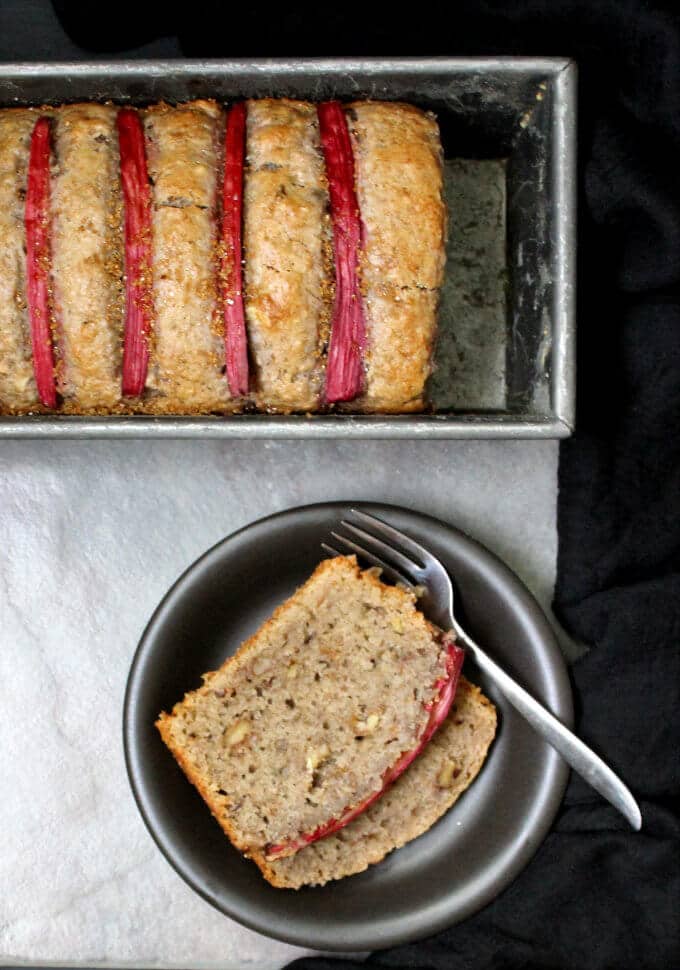 Photo of a vegan rhubarb bread baked in a loaf pan with two slices in a black plate.