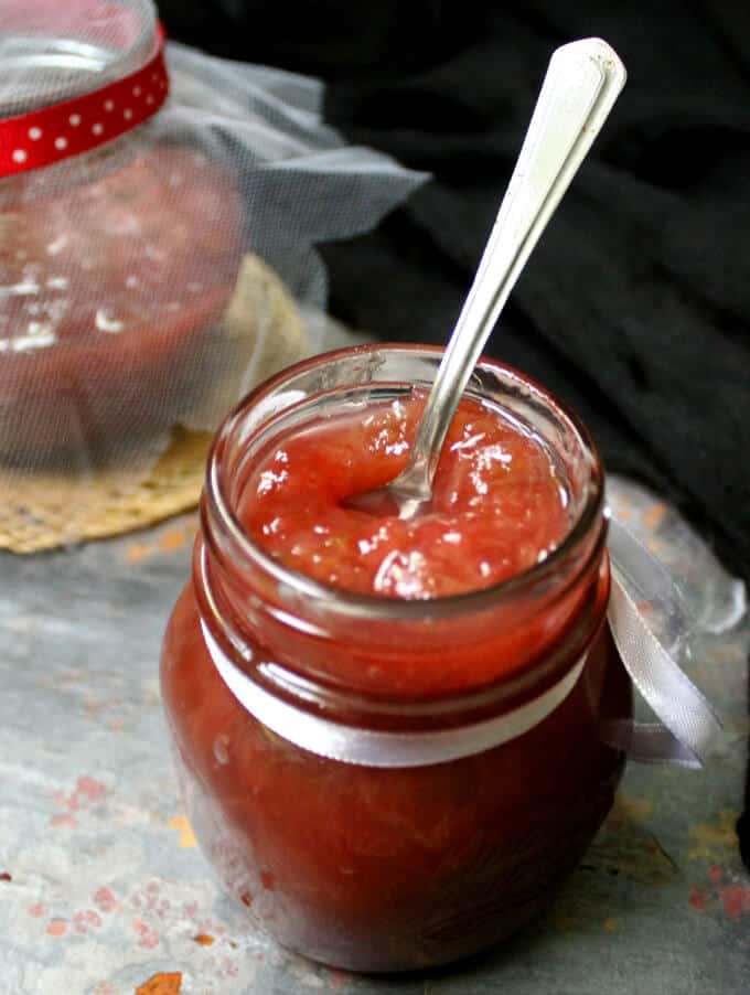Closeup shot of homemade rhubarb jam in a jar with a white ribbon and spoon.
