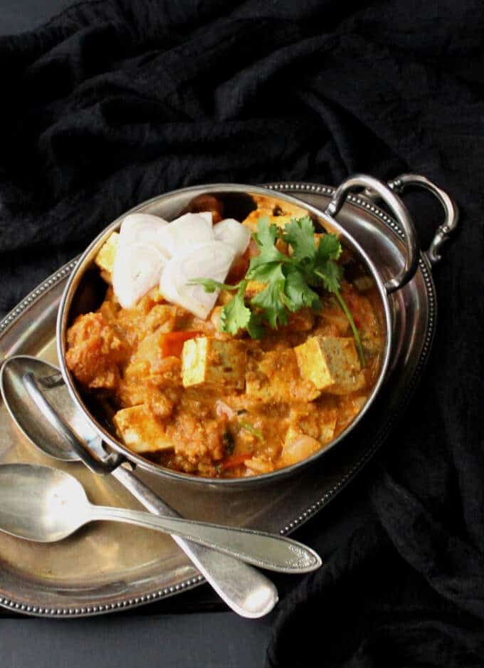 Vegan Kadai Tofu "Paneer" in kadhai with two spoons on the side and onion and cilantro garnish.