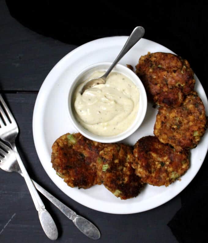 Vegan Maryland Crab Cakes in white plate with a white vegan tartar sauce and spoon in bowl.