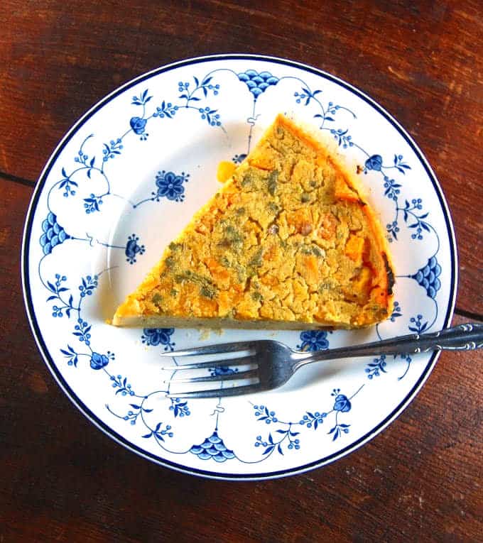 Photo of a slice of vegan butternut squash farinata on a blue and white china plate with a fork.