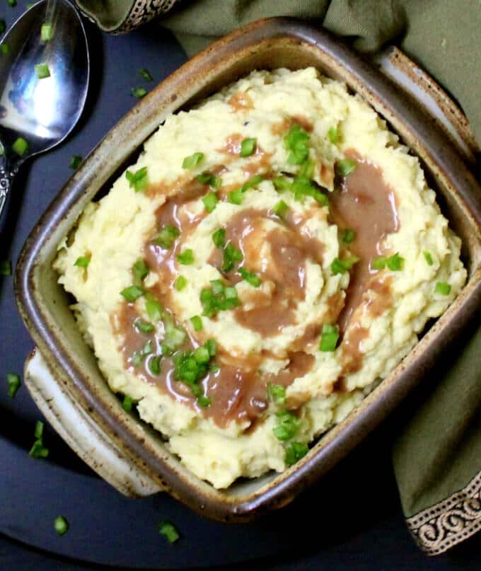 Overhead shot of vegan mashed potatoes with gravy and chives in a brown clay bowl.