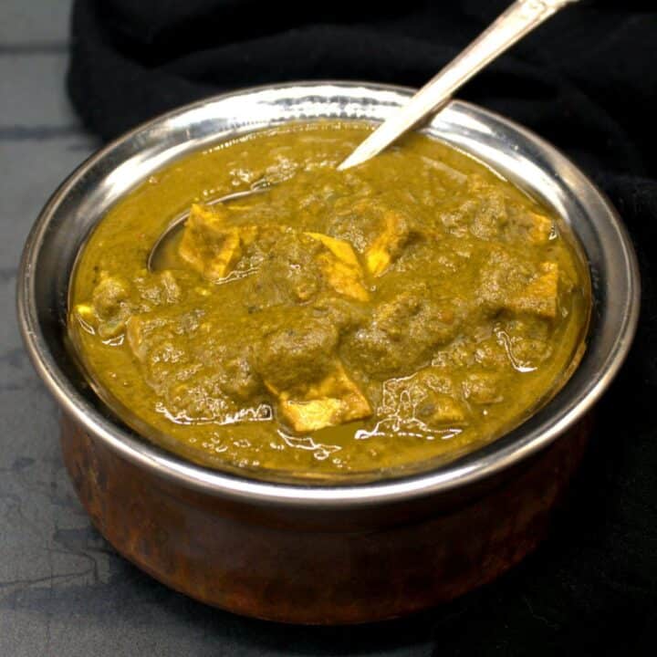Vegan palak paneer in an Indian copper degchi bowl with spoon.