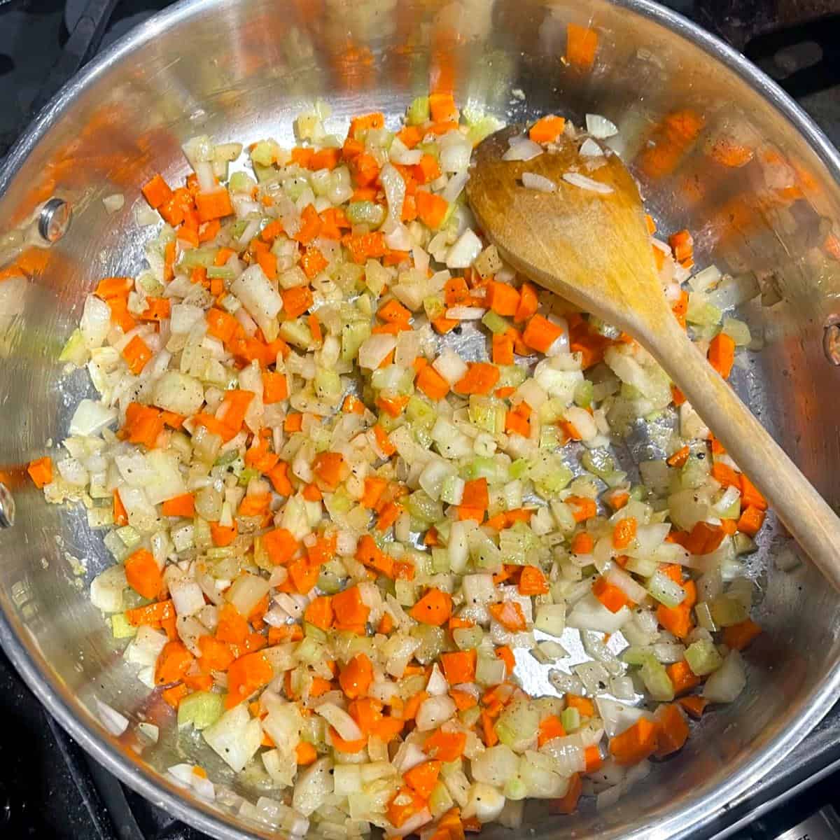 Garlic, carrots, onions and celery sauteing in pan with wooden ladle.