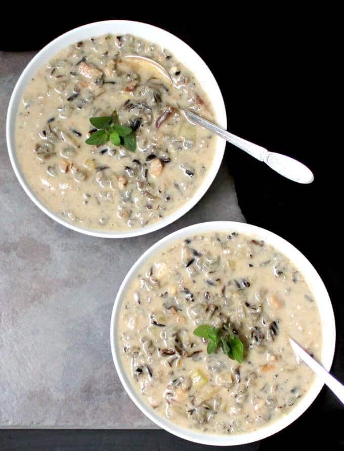 Two bowls of creamy mushroom chowder or bisque with flecks of white rice in two white bowls against a grey slate background and black in the background.