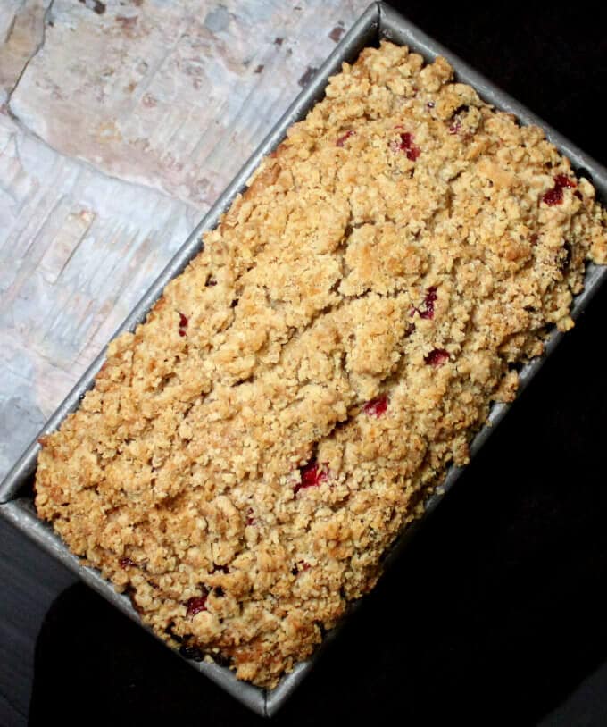 A vegan cranberry breakfast bread with streusel in a loaf pan against a grey slate and black background.