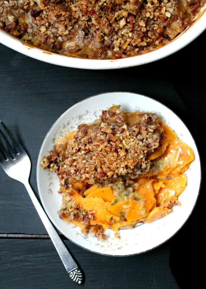 Vegan scalloped sweet potatoes in a bowl with a baking dish above it and a fork.
