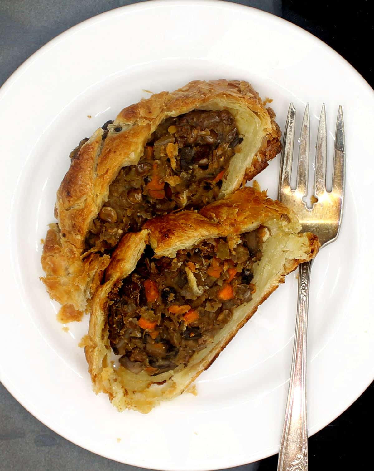 Vegan wellington slices on a white plate with fork.