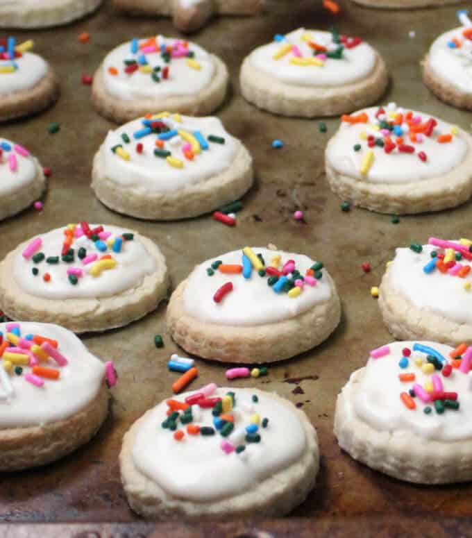 Vegan gf sugar cookies with icing and sprinkles on baking sheet.