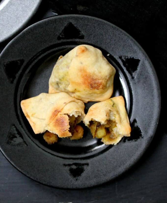 Cross section of a baked samosa with chickpeas and potatoes stuffed inside on a black plate against a black table