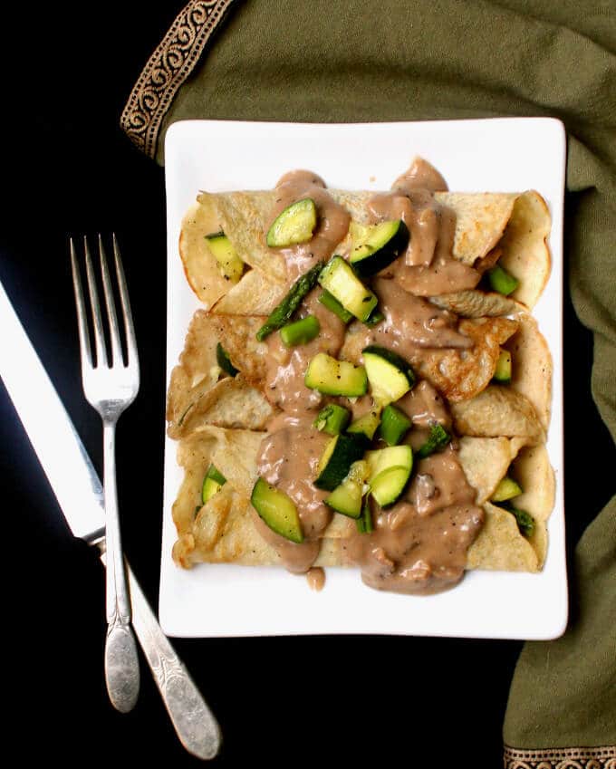 Savory Vegan Crepes with Mushroom Sauce in white plate with knife and fork and napkin.