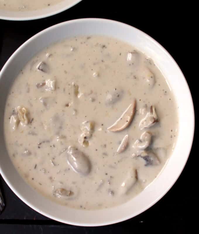 Overhead photo of a big white bowl of vegan cream of mushroom soup. Also partially visible is a second bowl of soup on a black background.