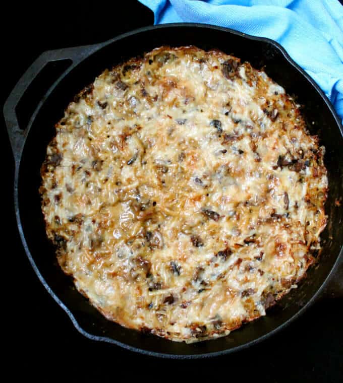 A bubbly, cheesy vegan Hash Brown Casserole baked in a cast iron skillet with cream of mushroom soup with a blue napkin beside it.