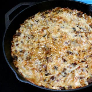 A bubbly, cheesy, golden vegan Hash Brown Casserole in a black cast iron griddle with a blue napkin next to it