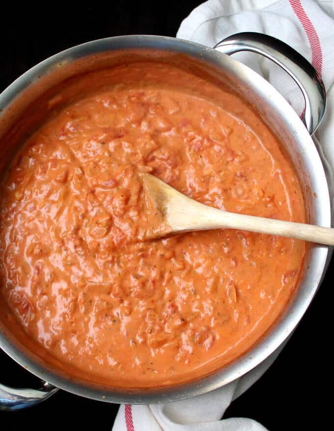 Creamy vegan vodka pasta sauce in a steel saucepan with a wooden ladle and a red and white napkin