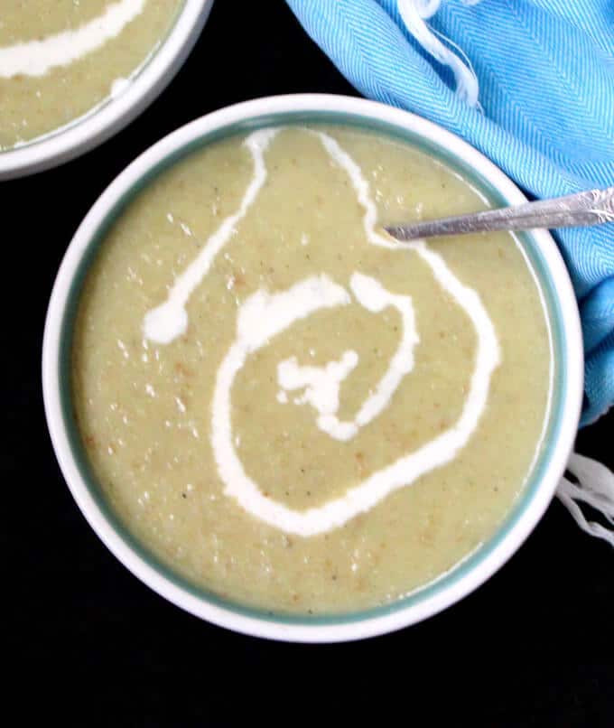Overhead photo of Vegan Irish Leek and Potato Soup with a cashew cream ganish in a blue and white bowl with soup spoon and a blue napkin behind.