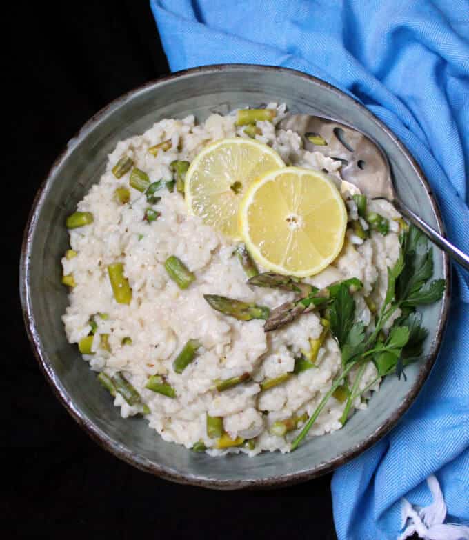 Asparagus risotto in bowl with slices of lemon and a sprig of parsley.