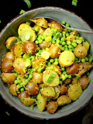 Vegan potato salad with green peas and turmeric in bowl with a spoon.