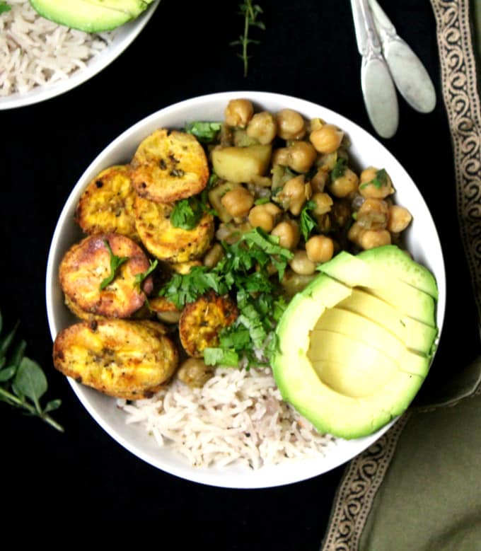 A delicious Caribbean Bowl with Coconut Rice, Chickpea Curry and Roasted Plantains and an avocado in white bowls.
