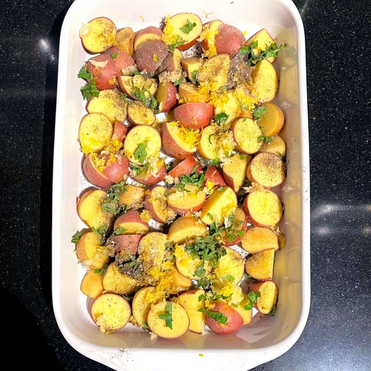 Oregano, salt, lemon zest and pepper added to potatoes in baking dish.