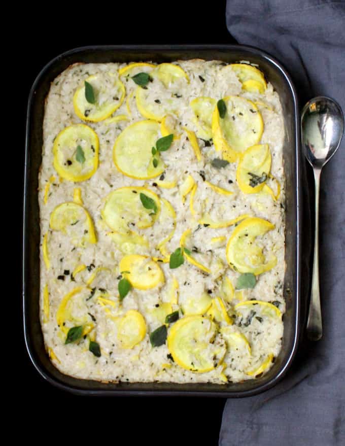 Savory Vegan Squash and Rice Pudding in brown baking dish with serving spoon on the side and a gray napkin next to it.