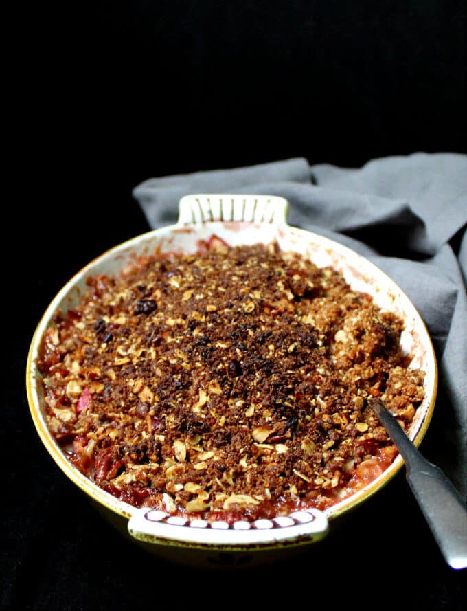 Front shot of a vegan rhubarb crisp in a yellow and white antique baking dish with a spoon.