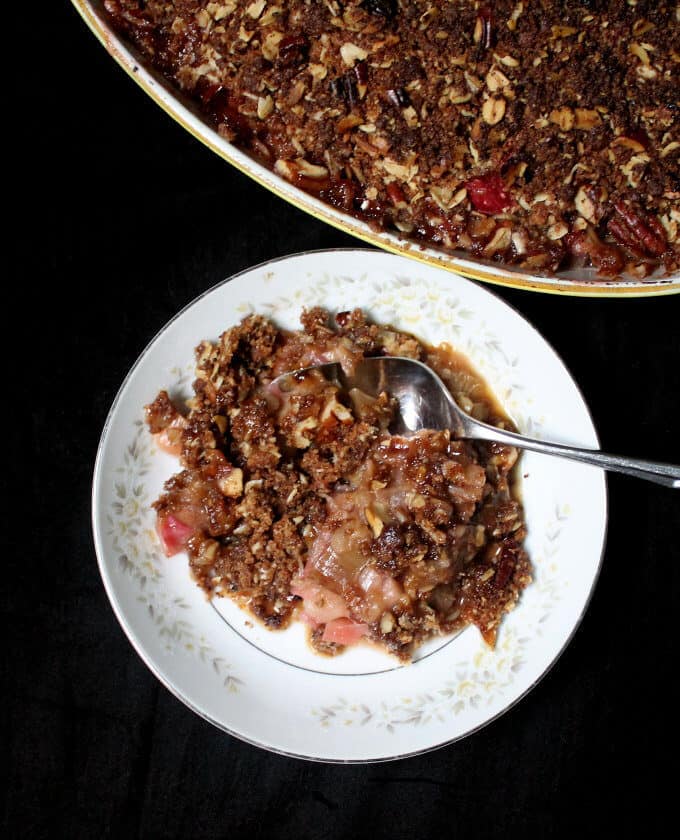 Photo of a piece of vegan rhubarb crisp with a gooey, jelly-like, tart rhubarb filling and a golden, delicious, oat and nut topping.