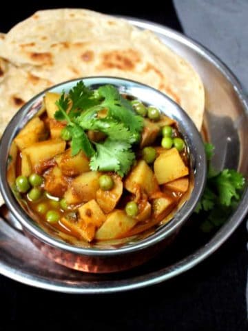 A close up of a copper and steel Indian handi bowl with aloo matar and chapatis