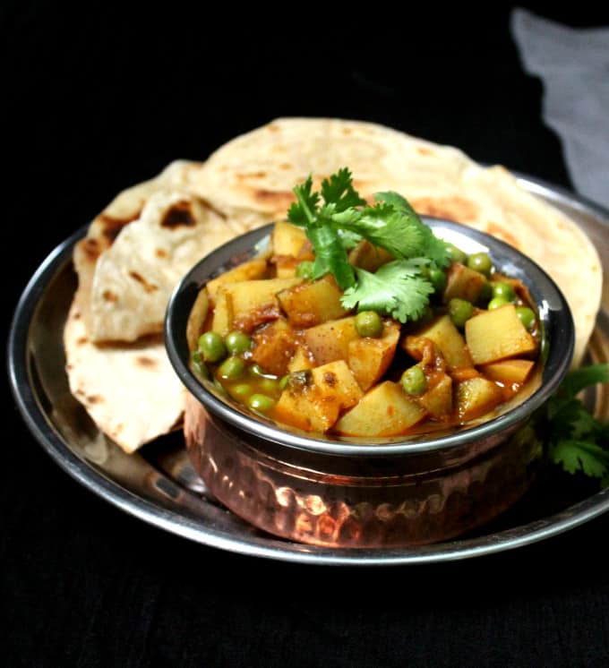 Frontal shot of a bowl of aloo matar with rotis or chapatis against a black background