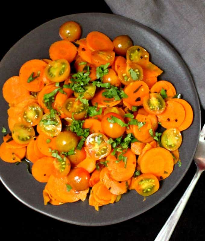 A partial top shot of a plate of curried carrot salad with cherry tomatoes and cilantro sprinkled on top