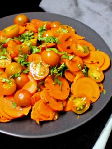 A partial front shot of a plate of curried carrot salad with cherry tomatoes and Indian spices and cilantro