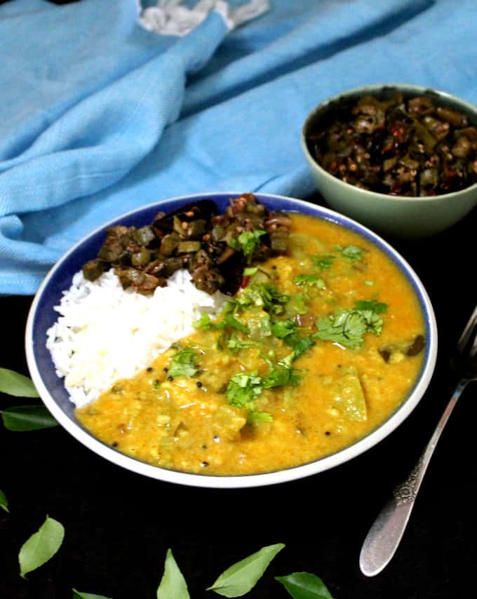 A front shot of the green tomato dal in a bowl with rice and okra subzi and a blue napkin behind.